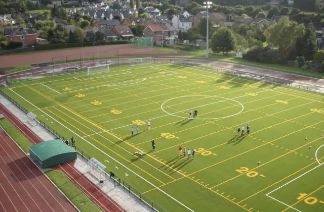 Vista aérea de un campo de césped artificial con líneas de juego, rodeado por una pista de atletismo