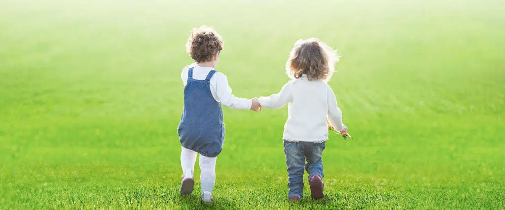 Dos niños caminando de la mano sobre el césped
