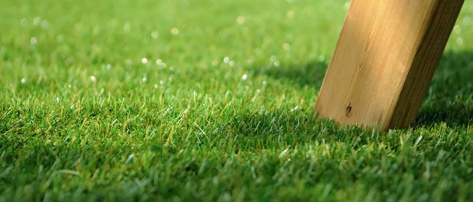 Primer plano de césped artificial con la pata de un mueble de madera