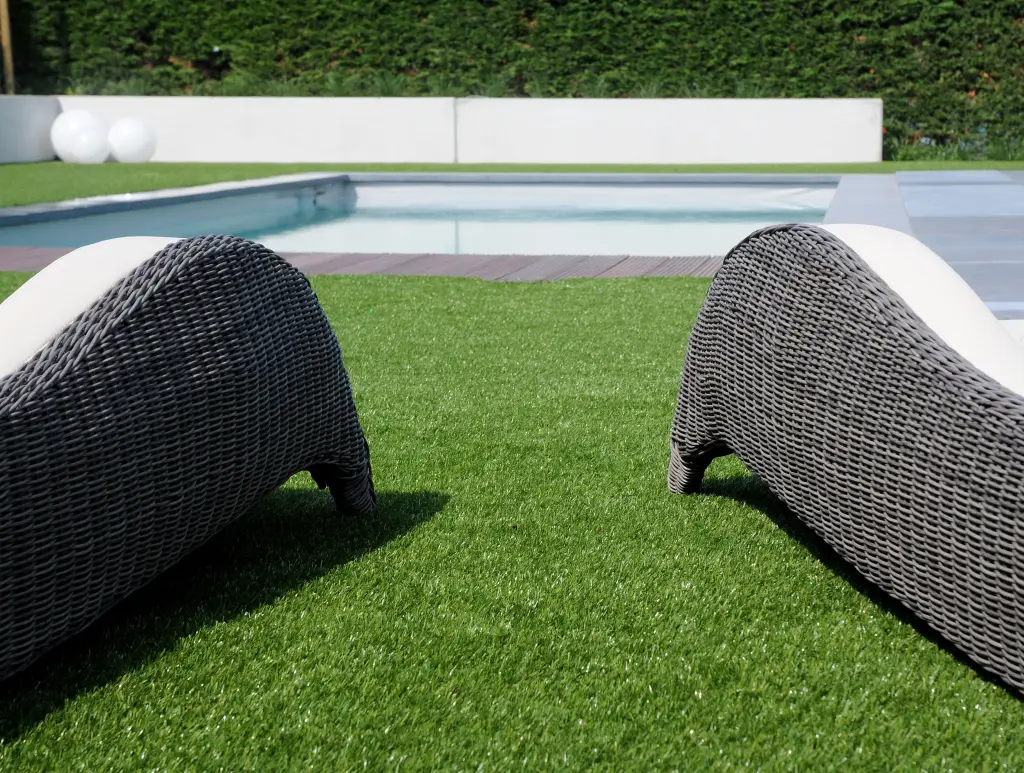Reposeras de mimbre sobre césped artificial junto a una piscina